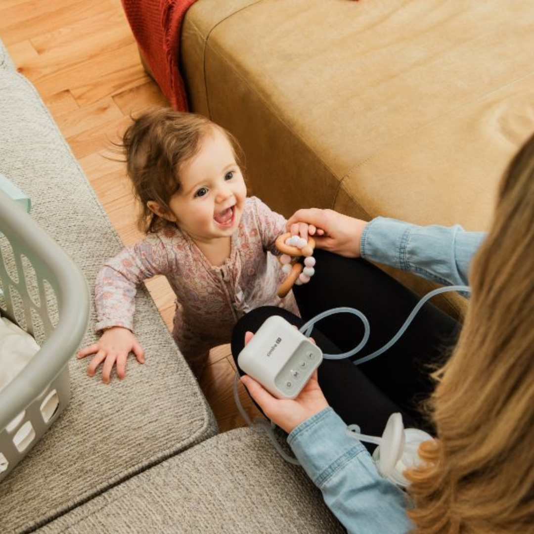 mom holding e1 breast pump with smiling baby in the background