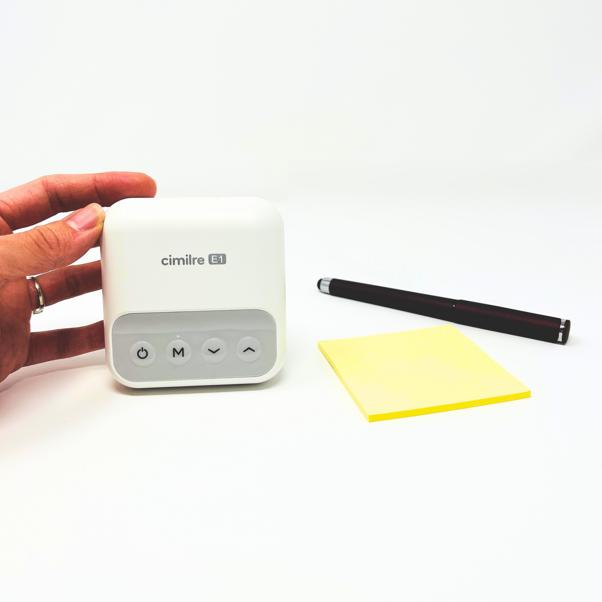 E1 breast pump held in hand next to sticky note and pen to show size comparison