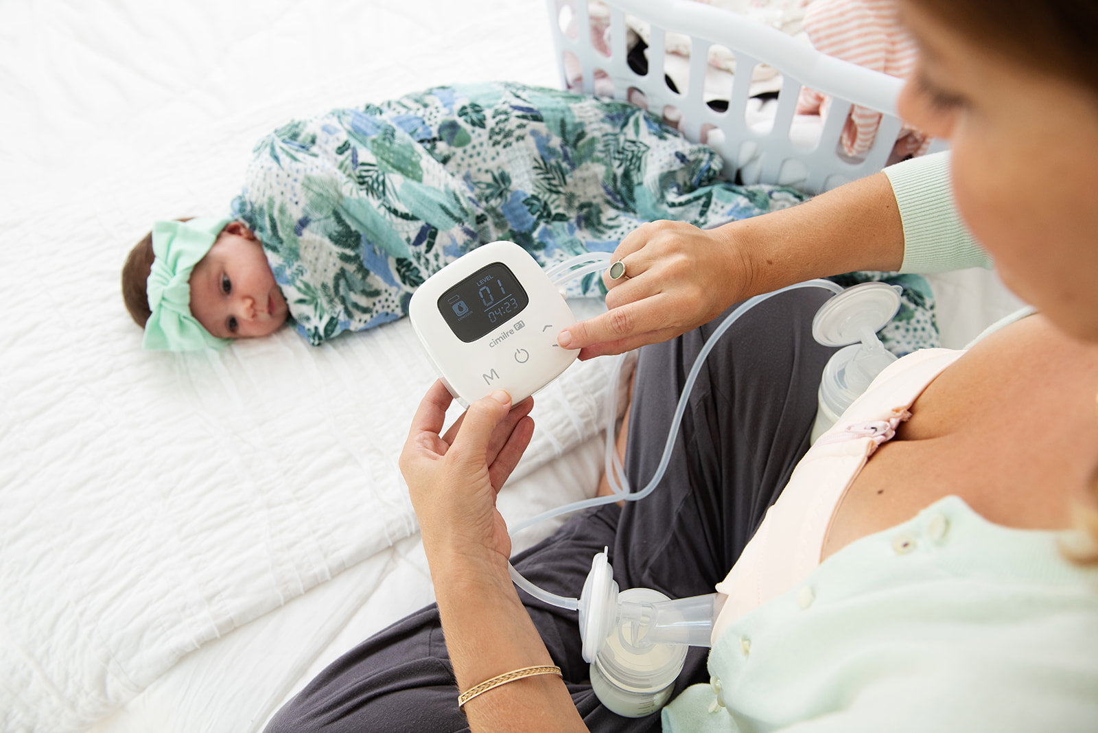 mom pumping with p1 breast pump with baby on bed next to laundry basket