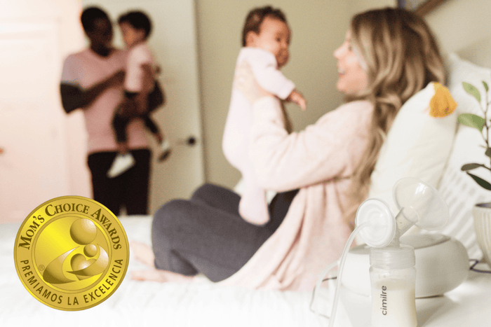Mom holding baby in foreground with dad holding toddler in background. S6+ with milk in collection kit on the end table.