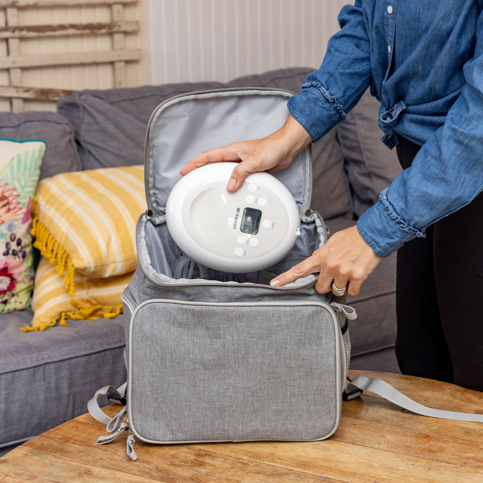 mom putting the S6+ into the journey backpack with a grey couch and yellow throw pillows in the background