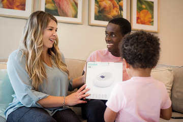 familly on couch, mom holding cimilre s6 breast pump in the box, toddler standing in front of parents