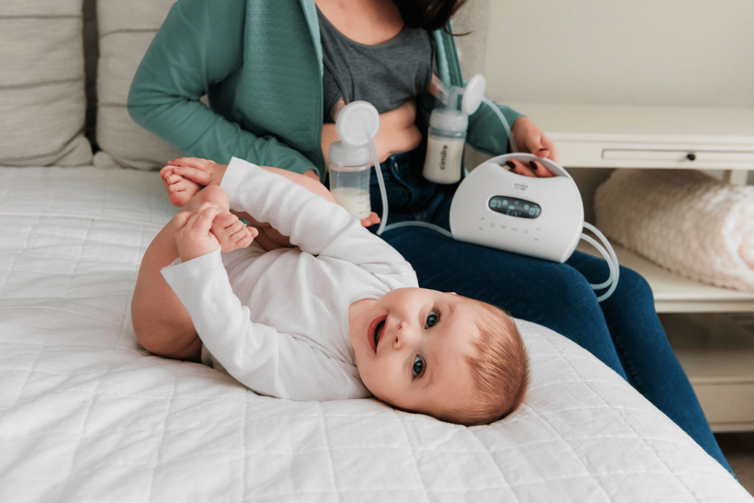 mom holding s7 dual pro pumping on a bed with baby next to her holding its feet